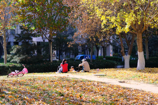A candid moment of a family laughing together in a sun-drenched park, surrounded by soft sand-colored autumn leaves.