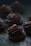Dark chocolate desserts are arranged on a textured wooden surface. The confectionery features swirled chocolate frosting with a small brown topping on each piece. The atmosphere is dimly lit, emphasizing the rich texture and color of the chocolate.