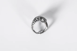 Close-up of a delicate silver ring with intricate design on a soft fabric background.