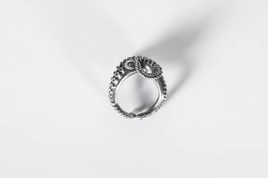 Close-up of a delicate silver ring with intricate design on a soft fabric background.