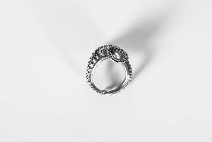Close-up of a delicate handmade silver ring resting on a white linen cloth, soft natural light highlighting its fine details.