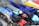 A close-up of a scattered collection of various pens, including ballpoint pens and highlighters. The pens are of different colors, primarily featuring blue, black, red, and yellow. Some pens have transparent bodies, revealing the ink inside, while others are opaque. The collection appears to be a mix of new and used pens, arranged haphazardly.