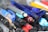 A close-up of a scattered collection of various pens, including ballpoint pens and highlighters. The pens are of different colors, primarily featuring blue, black, red, and yellow. Some pens have transparent bodies, revealing the ink inside, while others are opaque. The collection appears to be a mix of new and used pens, arranged haphazardly.