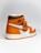 A stylish athletic shoe with a high-top design, featuring a combination of orange, brown, and white colors. The shoe displays a prominent logo on the side and a tag attached to the laces.
