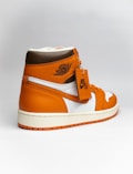 A stylish athletic shoe with a high-top design, featuring a combination of orange, brown, and white colors. The shoe displays a prominent logo on the side and a tag attached to the laces.