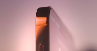 Close-up view of a sleek smartphone edge with metallic and glass surfaces reflecting soft ambient lighting.