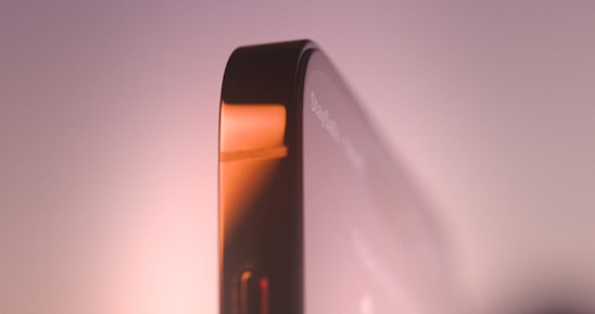 Close-up view of a sleek smartphone edge with metallic and glass surfaces reflecting soft ambient lighting.