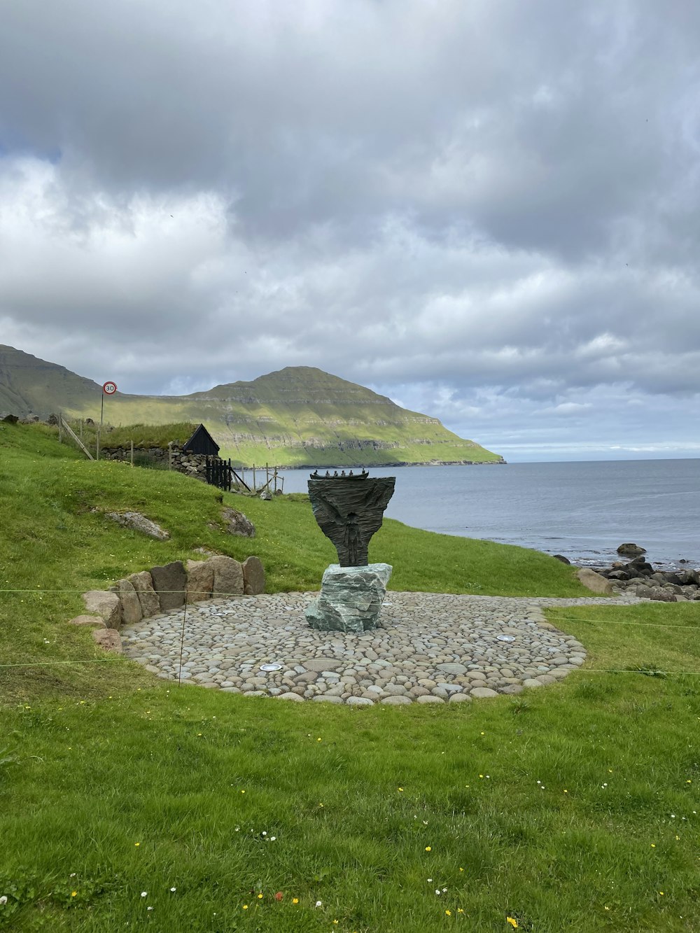 a stone fountain in a grassy area by a body of water