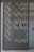 A decorative metal gate featuring an intricate geometric pattern is set within an entranceway. Behind the gate, there are signs indicating directions such as 'Exit' in red on the wall. The surrounding walls are light-colored, with a tiled surface visible.