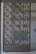 A decorative metal gate featuring an intricate geometric pattern is set within an entranceway. Behind the gate, there are signs indicating directions such as 'Exit' in red on the wall. The surrounding walls are light-colored, with a tiled surface visible.
