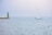 A sailboat with the words 'Ocean Team' on its side is moving across a calm sea. A lighthouse stands on a pier to the left, with a slightly overcast sky in the background.