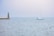 A sailboat with the words 'Ocean Team' on its side is moving across a calm sea. A lighthouse stands on a pier to the left, with a slightly overcast sky in the background.