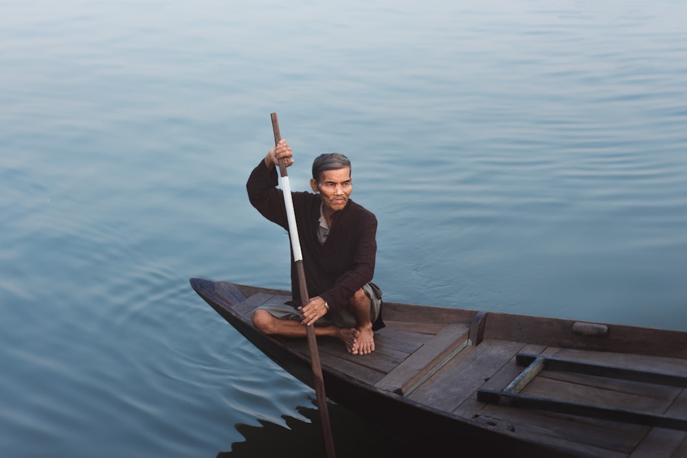 a man sitting on a dock holding a stick