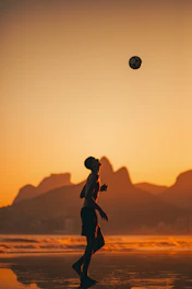 Dynamic shot of a soccer player mid-air striking the ball during a sunset match.
