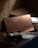 A close-up view of a copper-colored metallic card with the brand logo 'Axwell' displayed on its surface. The card is situated among tools, including a handle with 'U.N.T-D' engraved on it and a wooden plank. Dim lighting accentuates the textures and provides a warm, rustic ambiance.
