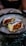 Two oysters served on a bed of ice in a decorative bowl. The oysters contain a red sauce and a slice of cucumber.