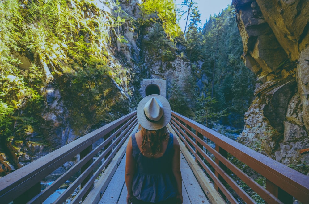 a person wearing a hat and standing on a bridge over a waterfall