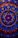An intricate circular mandala pattern with vibrant colors including red, blue, gold, and pink. The design features concentric circles, floral motifs, and dots that create a symmetrical and ornate look. Elements radiate from the center and are repeated rhythmically, forming a harmonious and elaborate design.
