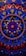 An intricate circular mandala pattern with vibrant colors including red, blue, gold, and pink. The design features concentric circles, floral motifs, and dots that create a symmetrical and ornate look. Elements radiate from the center and are repeated rhythmically, forming a harmonious and elaborate design.