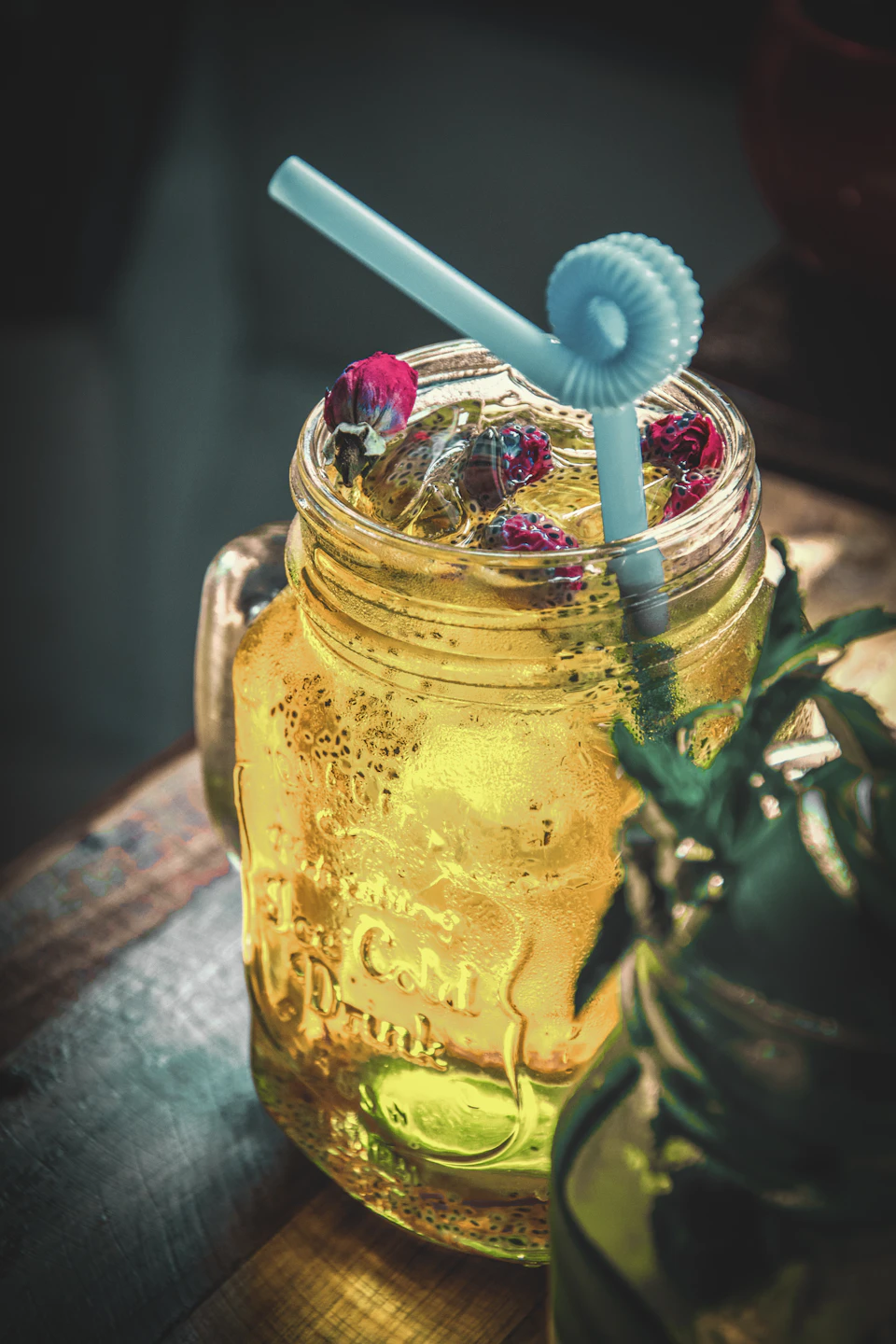 Tall glass jar filled with yellow liquid, resting on a wooden table, surrounded by jars