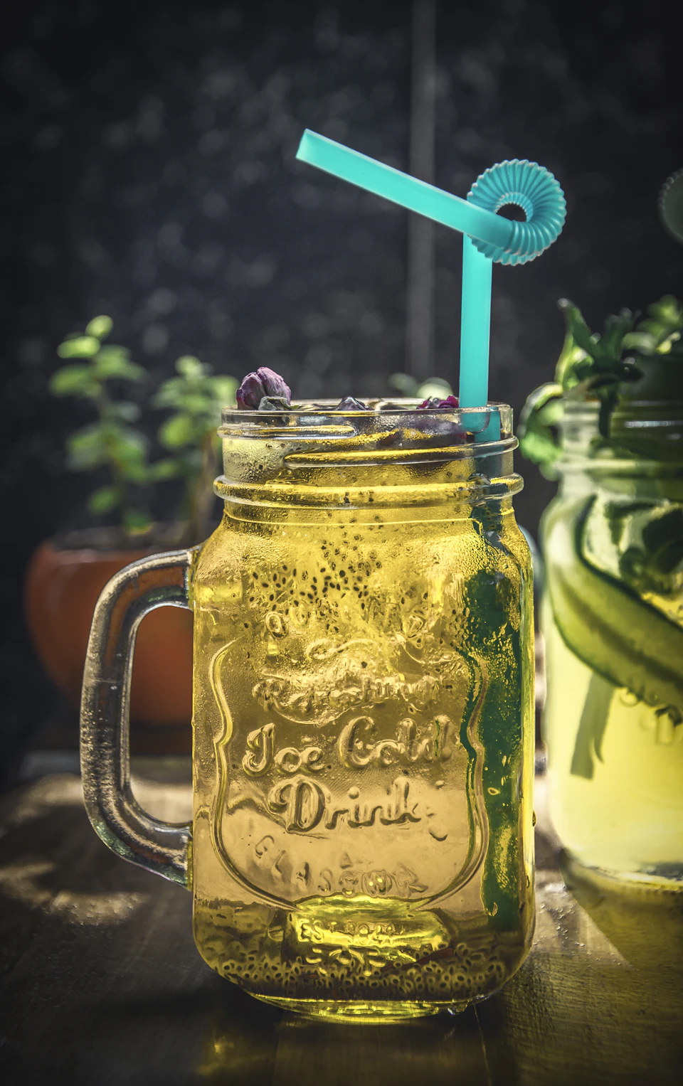 Tall glass jar filled with ice-cold lemonade on wooden table with blue straw handle