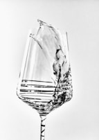 A clear, intricately designed wine glass captures the motion of liquid splash within it, showcasing elegant lines and patterns in a grayscale palette.