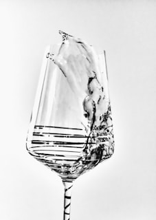 A clear, intricately designed wine glass captures the motion of liquid splash within it, showcasing elegant lines and patterns in a grayscale palette.