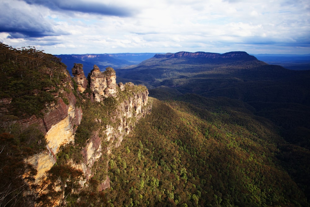 a rocky cliff with a valley below with Blue Mountains in the background