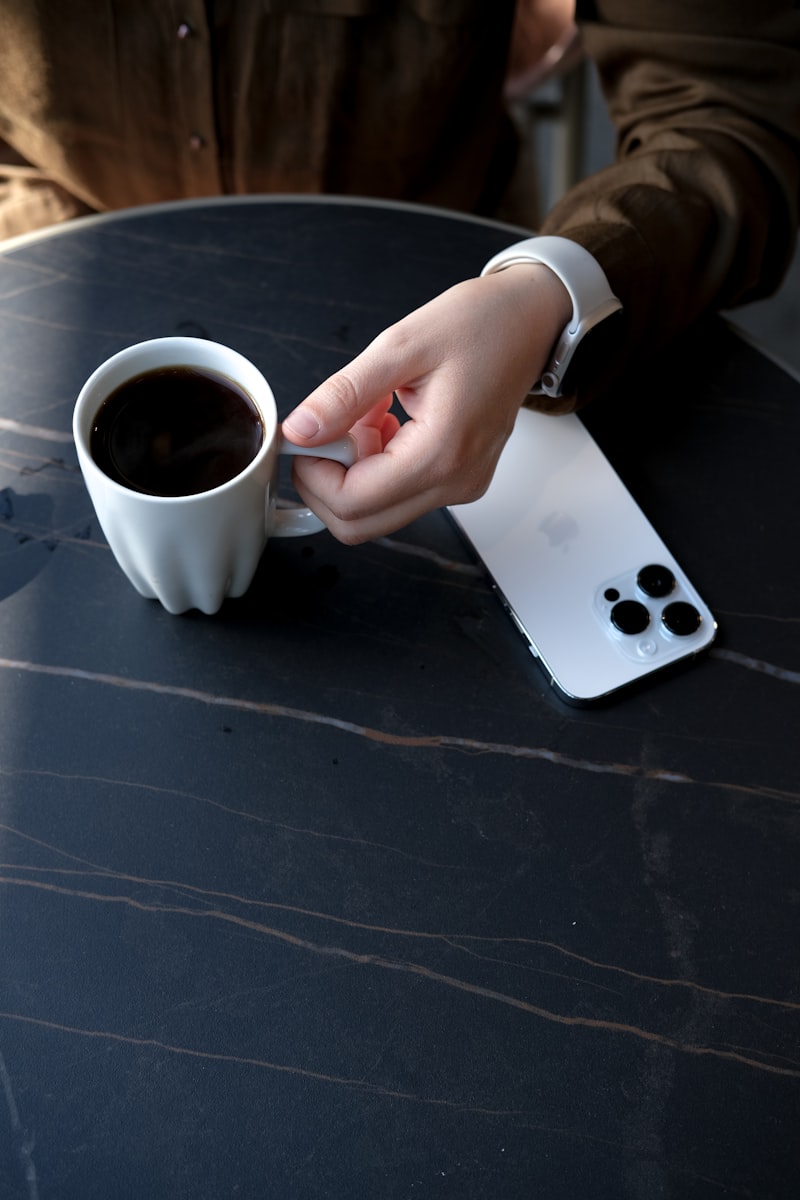 Hand holding smartphone with banking app and coffee cup