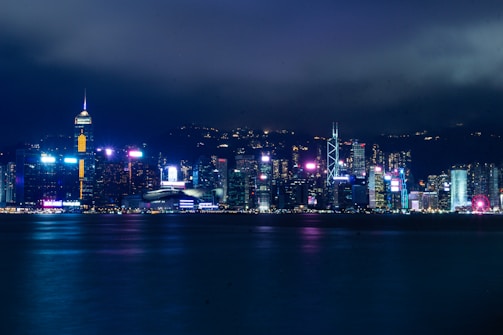 A moody photo of a city skyline at night with silver lights reflecting on glass buildings