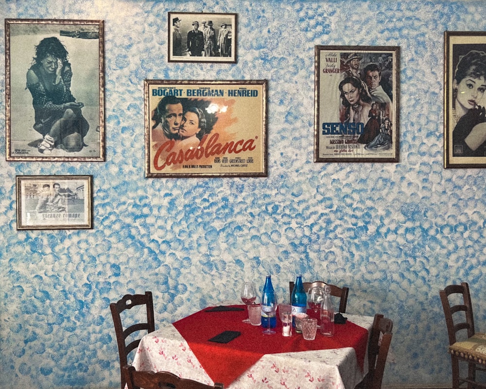 a table with a red tablecloth and chairs with pictures on the wall