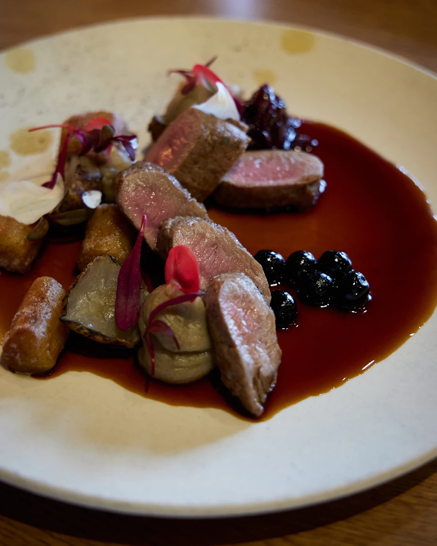 Slices of seared game meat plated with dark berry sauce and lingonberries