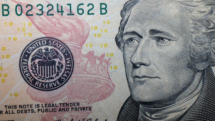 A close-up of a US Federal Reserve Note featuring intricate line work and detailed imagery. The portrait of a historical figure is prominent on the right, while a portion of the Federal Reserve emblem with an eagle is visible on the left. Small '10' numerals are scattered across the background.