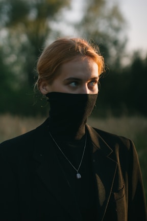 A casual outfit featuring a deep black turtleneck and brown trousers, posed outdoors with soft natural light.
