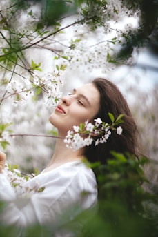 A peaceful woman praying with hands clasped, surrounded by blue and pink blossoms.
