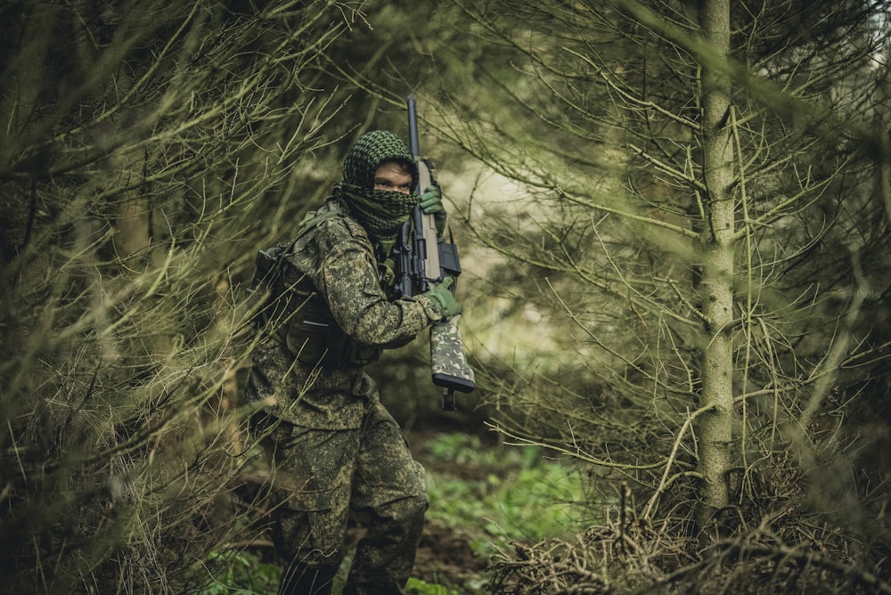 a person in camouflage holding a gun in the woods