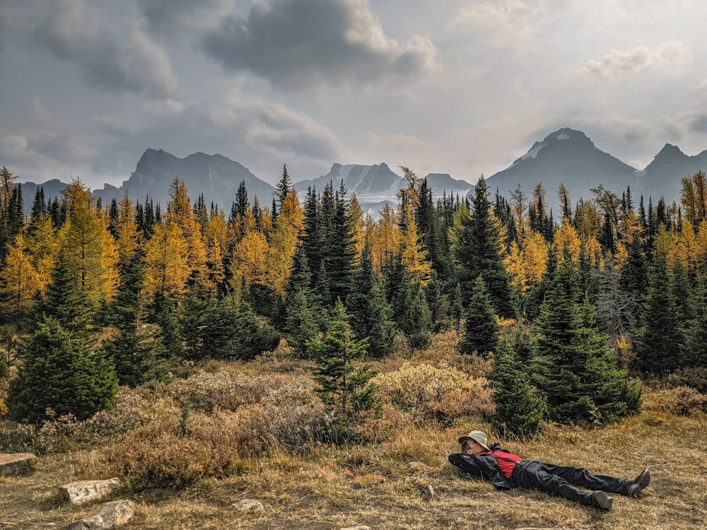 a person lying on the ground with trees and mountains in the background