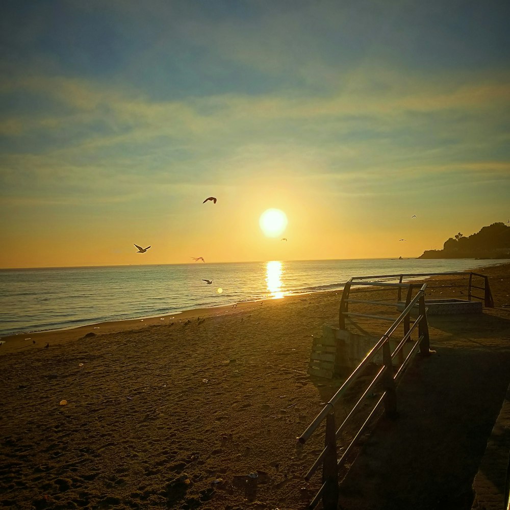 a beach with a railing and a body of water with a sunset