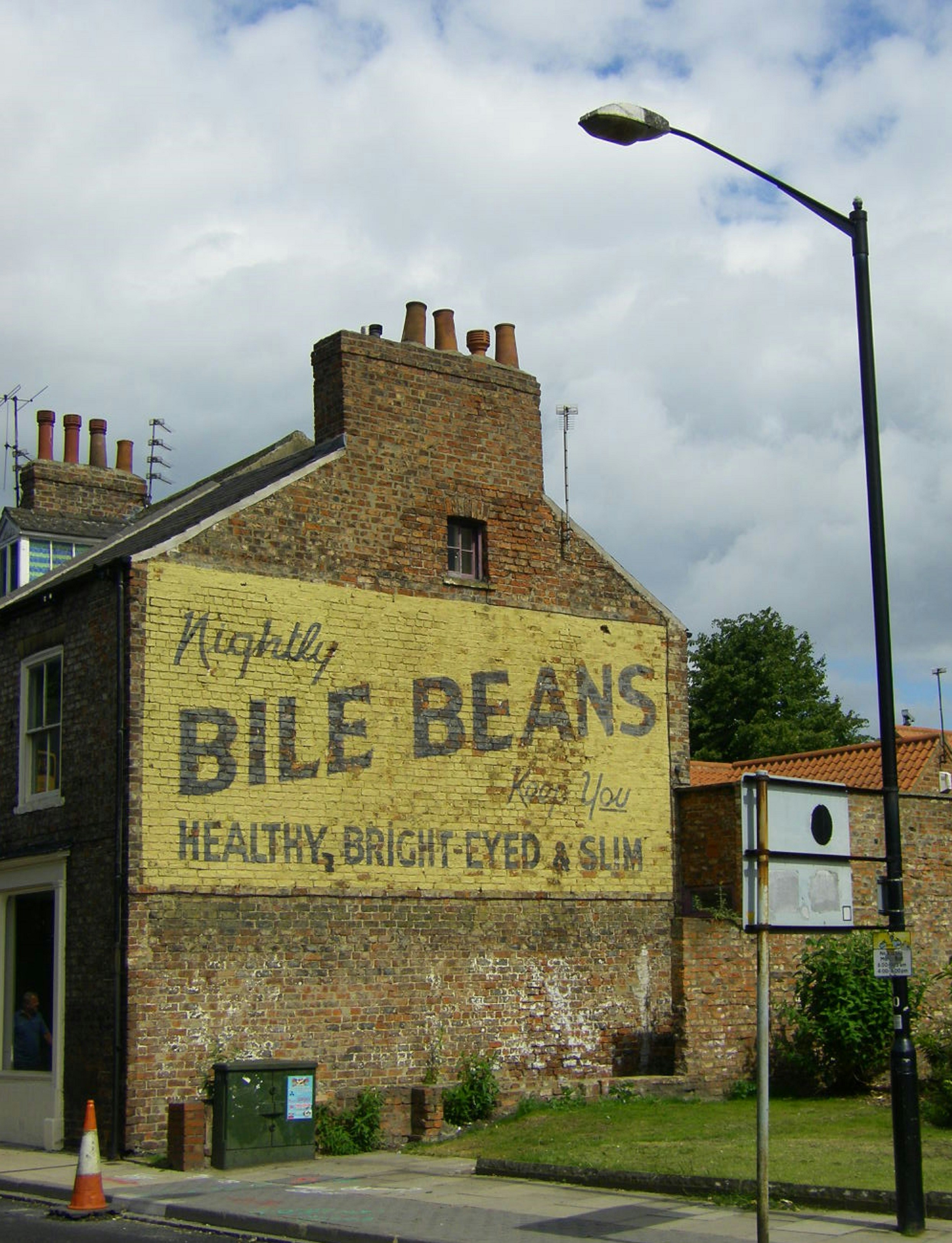 Old Bile Beans advertisement painted in yellow on old brown brick wall side of building.