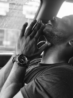 A person with eyes closed and hands clasped near their face, wearing a wristwatch, appears to be in a reflective or meditative state. The black and white filter adds a contemplative and calm atmosphere.