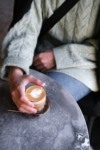 Casual woman wearing tailored high-waisted pants paired with a cozy knit sweater, sitting at a cafe table.