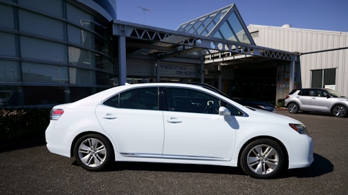 A sleek silver sedan parked in front of a modern office building under a clear blue sky.