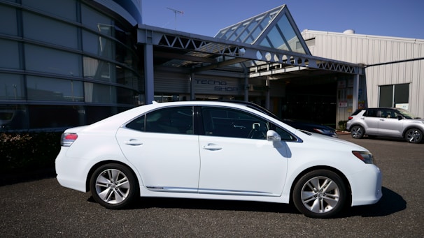 A shiny red sedan parked in front of a modern building under clear blue skies.