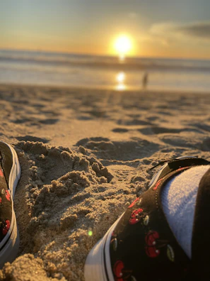 Sunset scene with a pair of aqua shoes on the sand beside a beach towel and summer outfit.