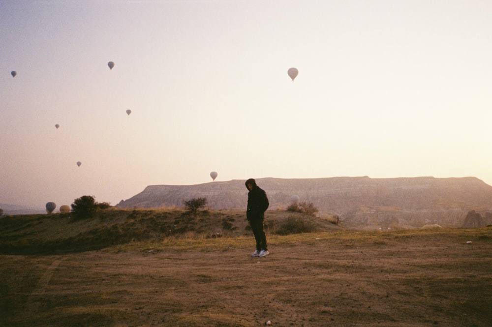 a man standing in a field with hot air balloons in the sky