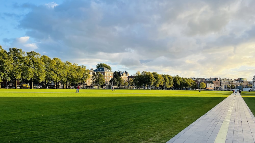 a large green field with trees and buildings in the background