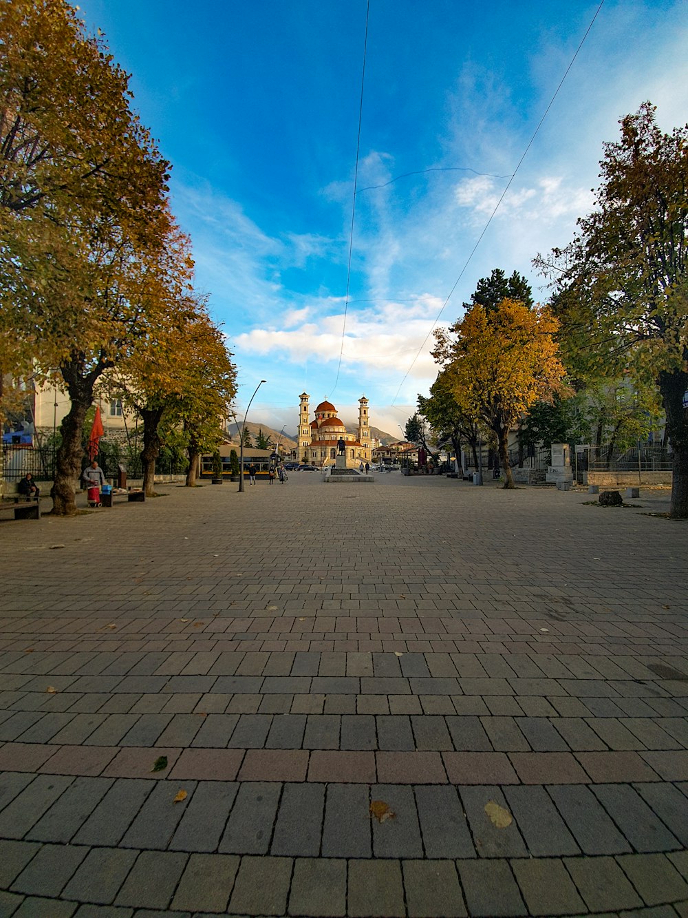 a brick walkway with trees and buildings in the background