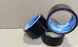 Three rolls of black adhesive tape with blue inner linings are placed on a textured cardboard surface. The rolls are partially unwound, and each displays the brand name 'Stefil' on the inside.