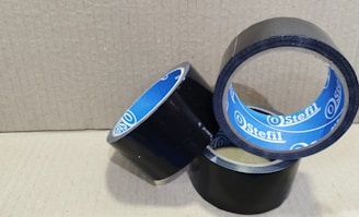 Three rolls of black adhesive tape with blue inner linings are placed on a textured cardboard surface. The rolls are partially unwound, and each displays the brand name 'Stefil' on the inside.