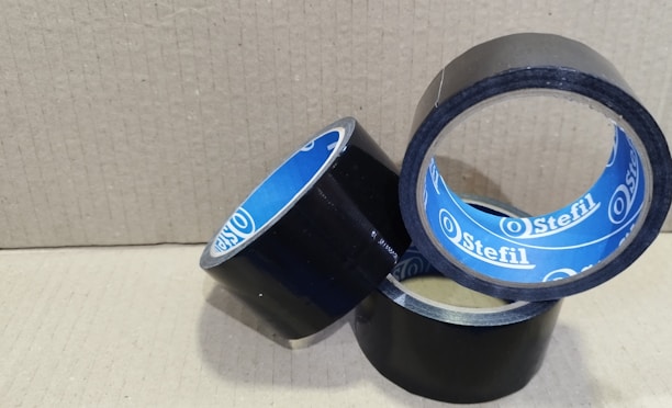 Close-up shot of strong adhesive tapes in classic blue and black colors, one roll partially unspooled on a clean white surface.